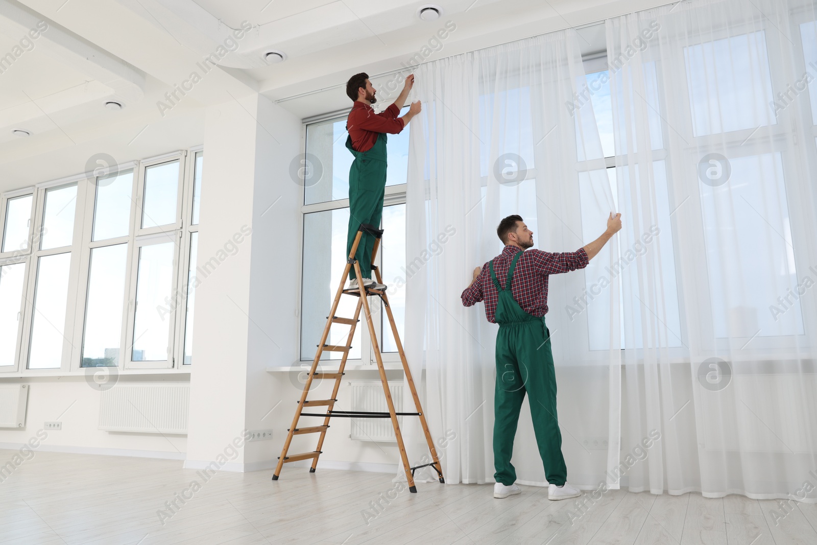 Workers in uniform hanging window curtain indoors Photo of Workers in uniform hanging window curtain indoors