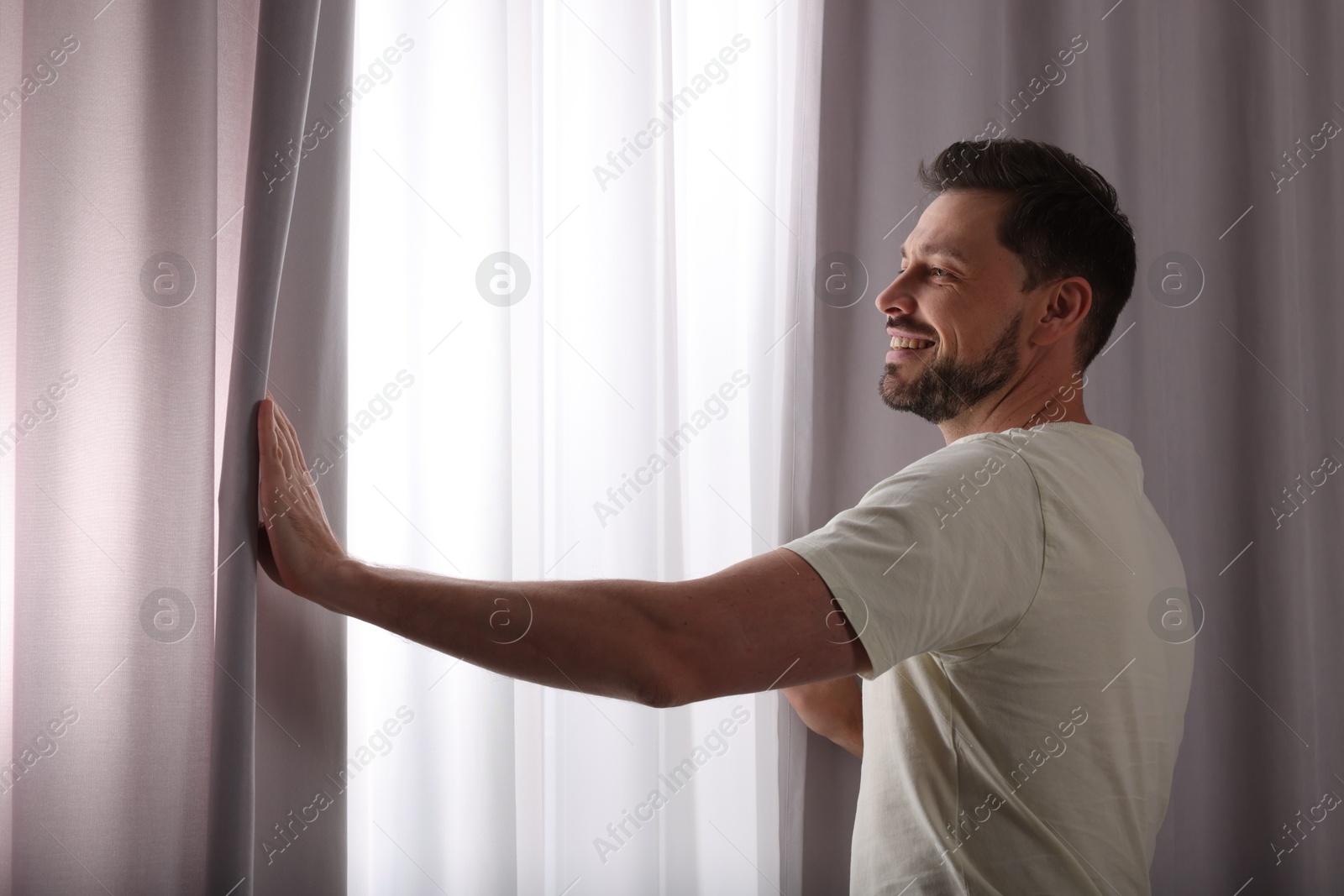 Happy man opening window curtains at home Photo of Happy man opening window curtains at home