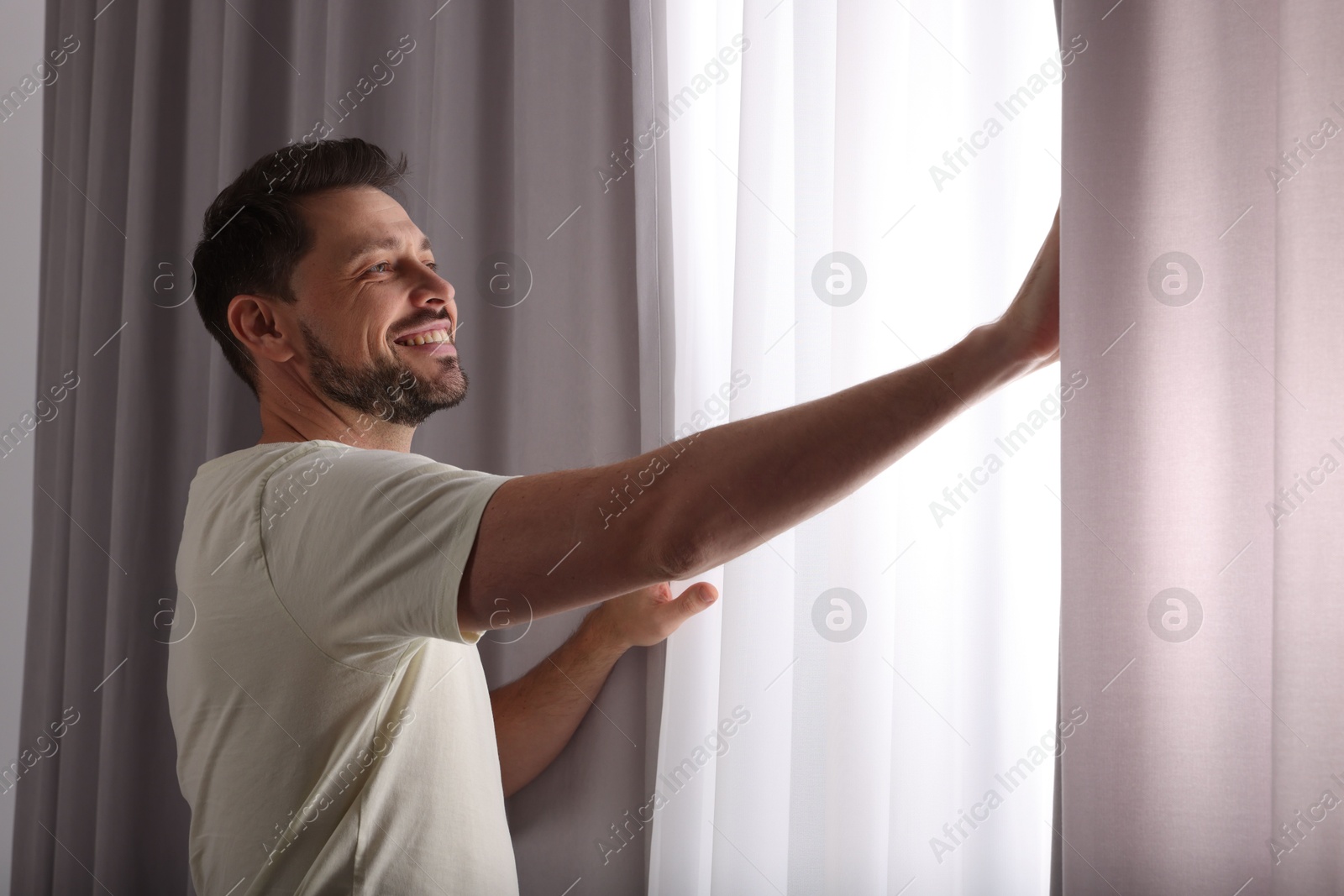 Happy man opening window curtains at home Photo of Happy man opening window curtains at home