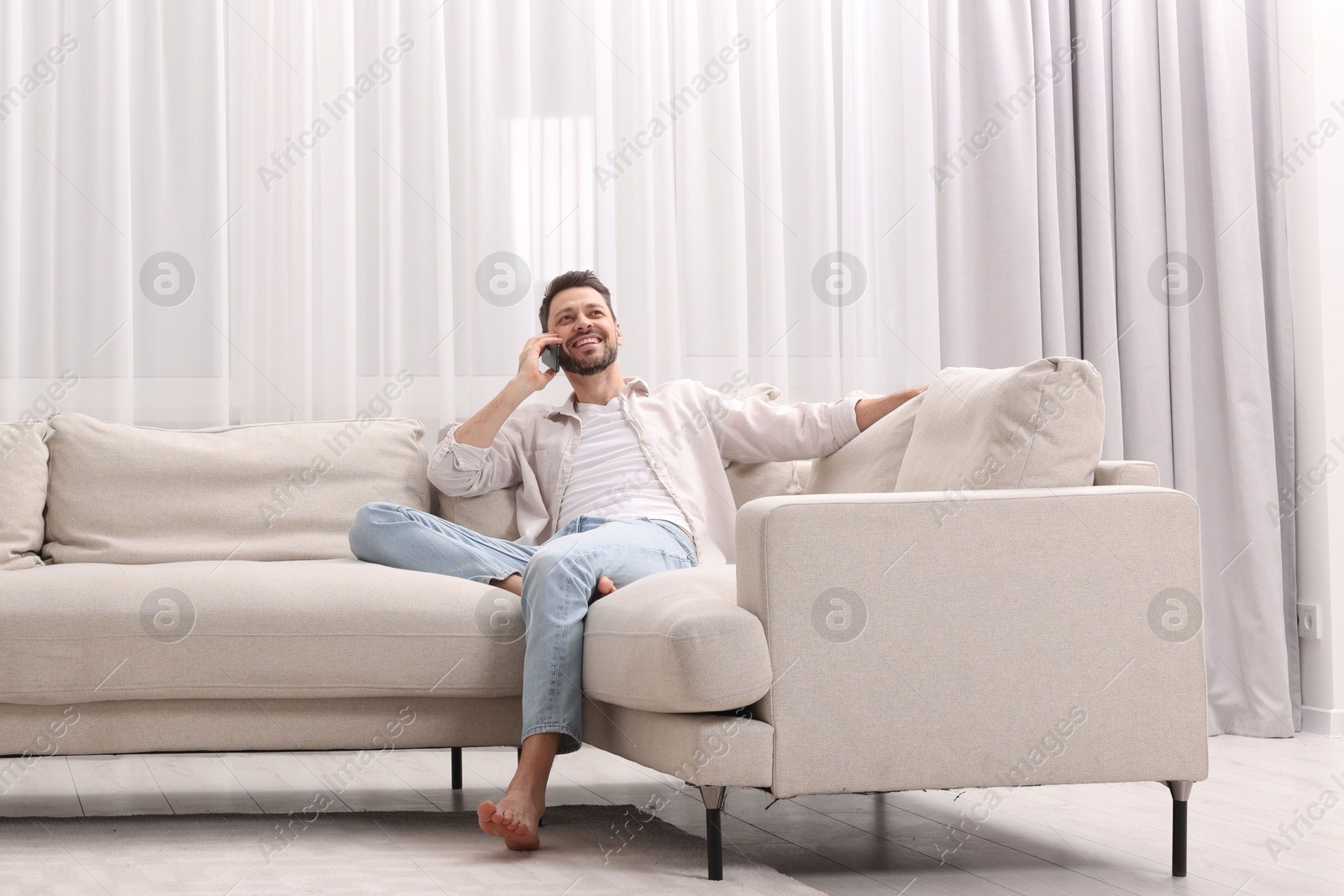 Man talking smartphone near window with beautiful curtains in living room Photo of Man talking smartphone near window with beautiful curtains in living room