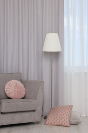 Photo of Stylish room interior with comfortable armchair and beautiful window curtains