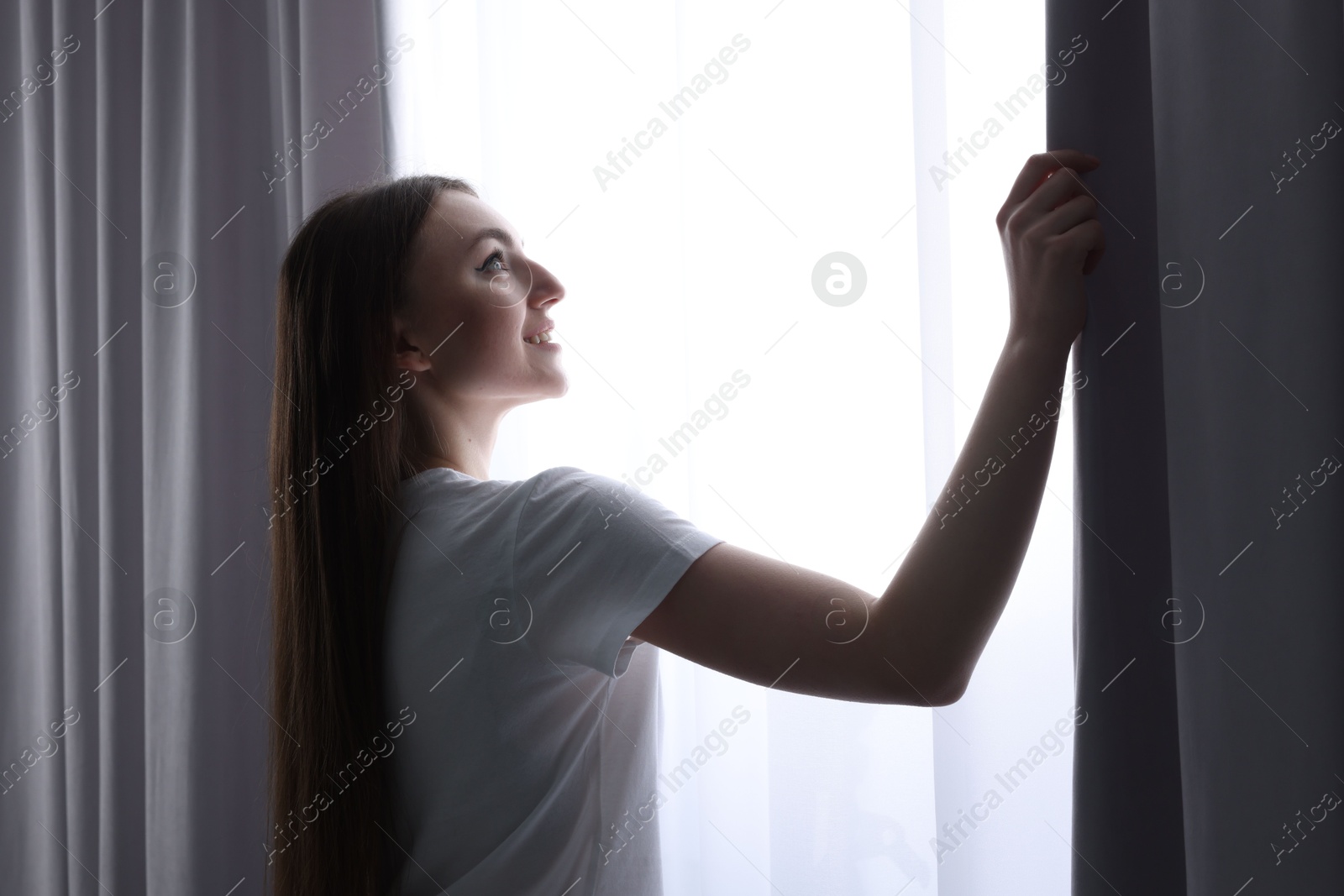 Happy woman opening stylish curtains at home Photo of Happy woman opening stylish curtains at home