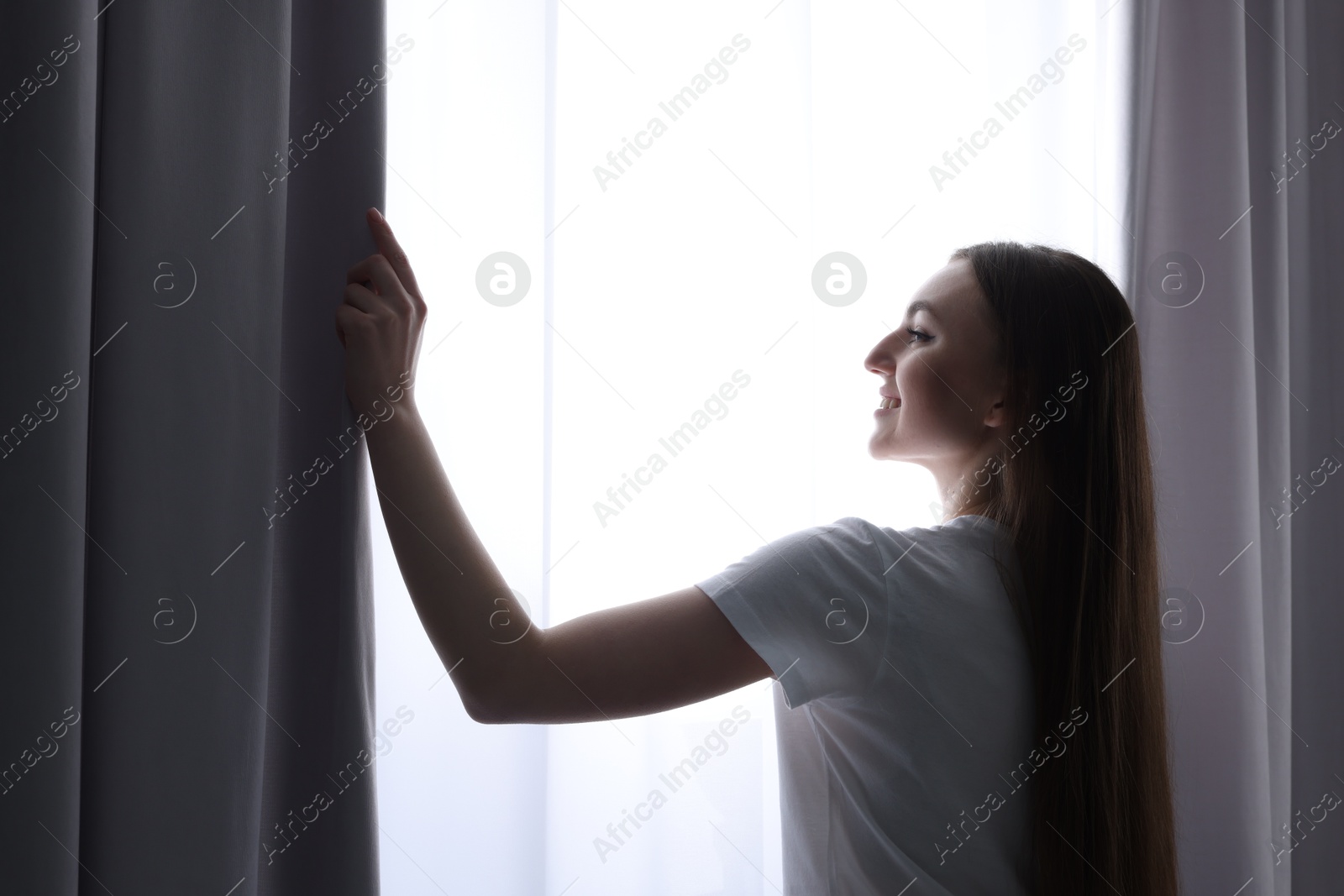 Happy woman opening stylish curtains at home Photo of Happy woman opening stylish curtains at home