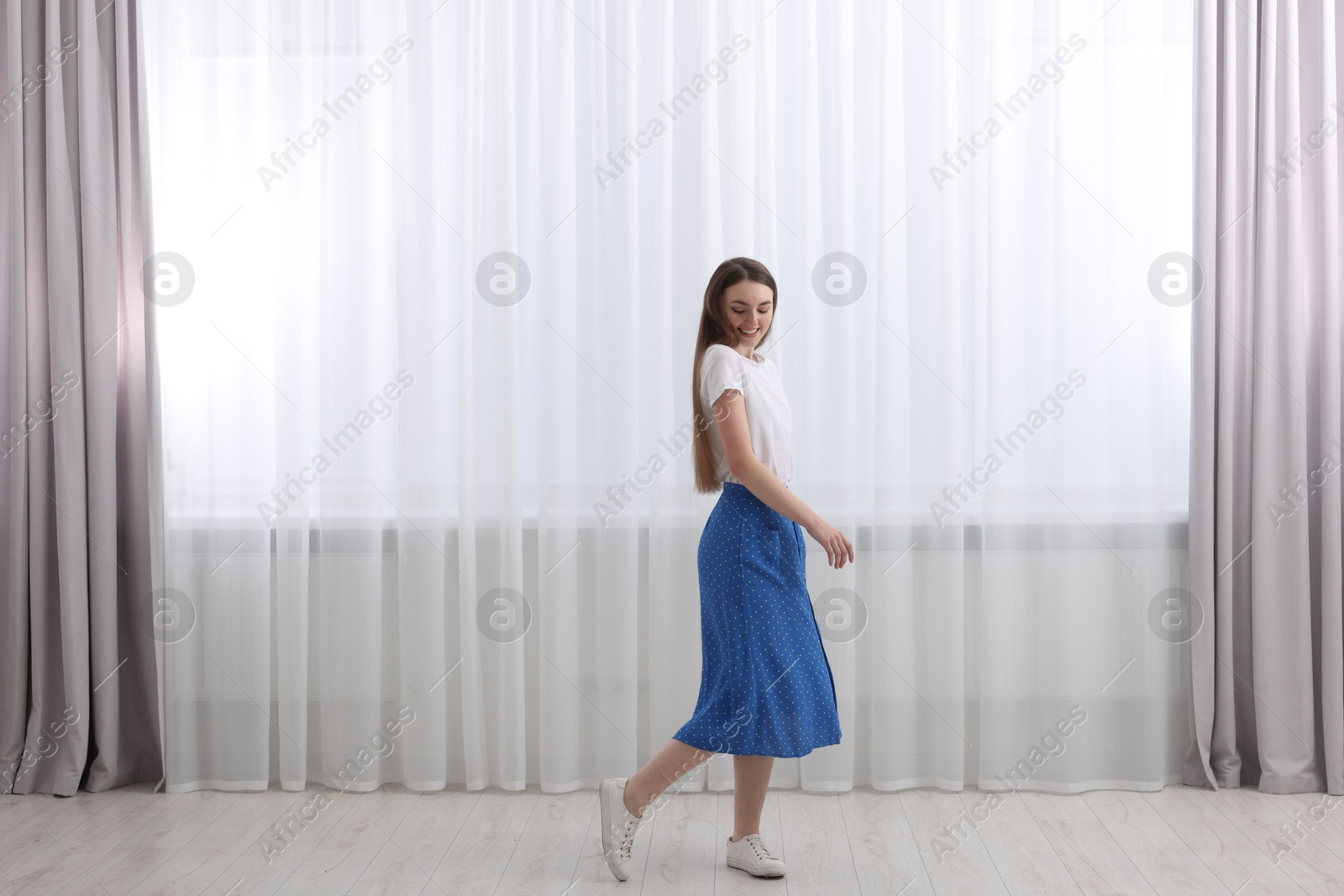 Woman standing near window with stylish curtains at home. Space for text Photo of Woman standing near window with stylish curtains at home. Space for text