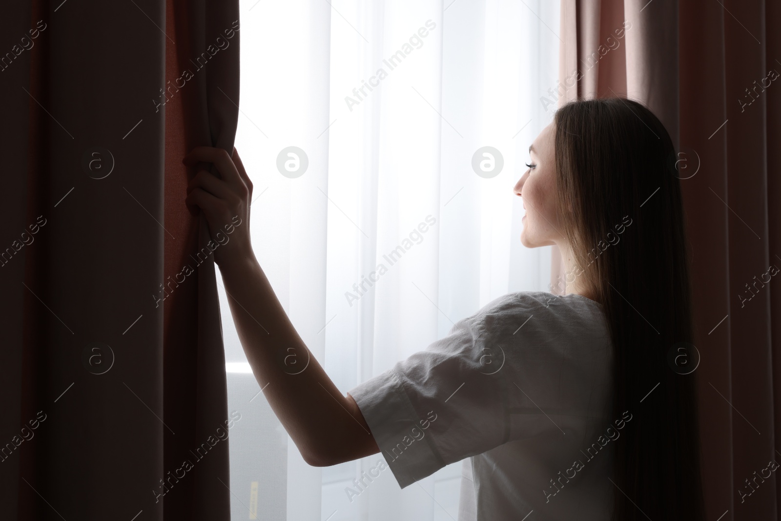 Happy woman opening stylish window curtains at home Photo of Happy woman opening stylish window curtains at home
