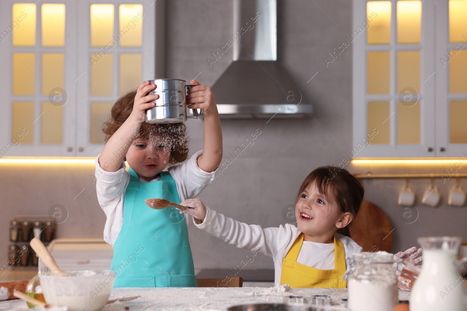 Cooking recipe. Cute children sieving flour at table in kitchen Photo of Cooking recipe. Cute children sieving flour at table in kitchen