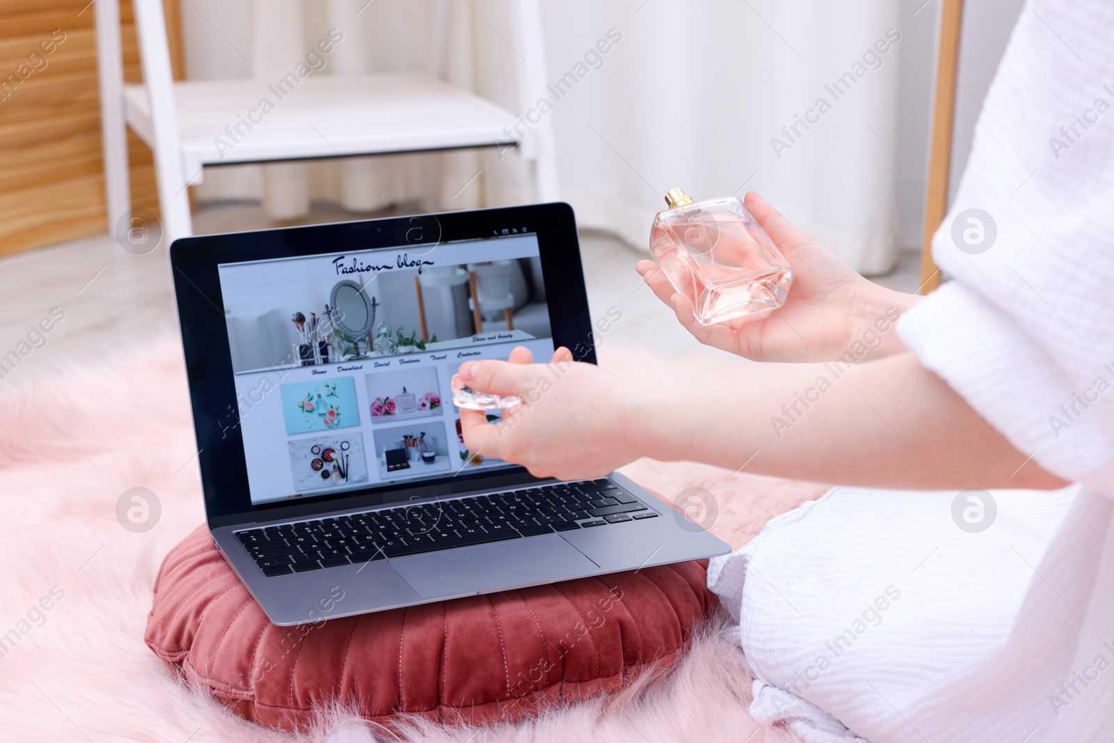 Blogger holding perfume near laptop with fashion blog web site on floor indoors, closeup Photo of Blogger holding perfume near laptop with fashion blog web site on floor indoors, closeup