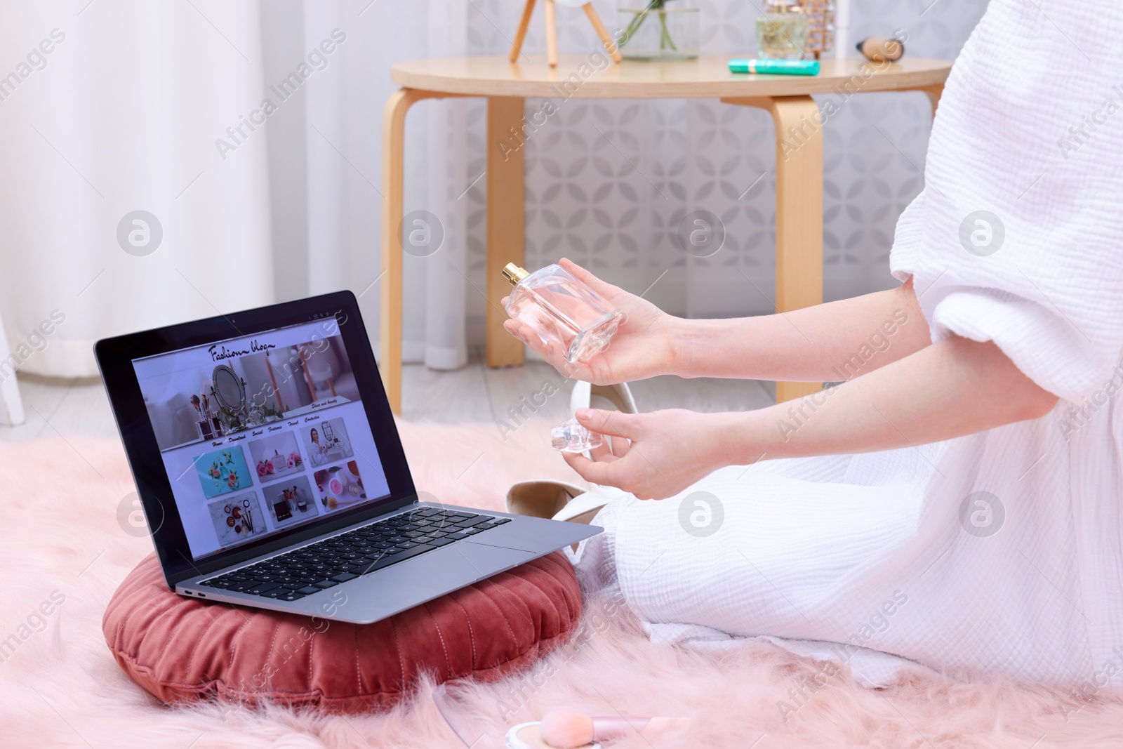 Blogger holding perfume near laptop with fashion blog web site on floor indoors, closeup Photo of Blogger holding perfume near laptop with fashion blog web site on floor indoors, closeup