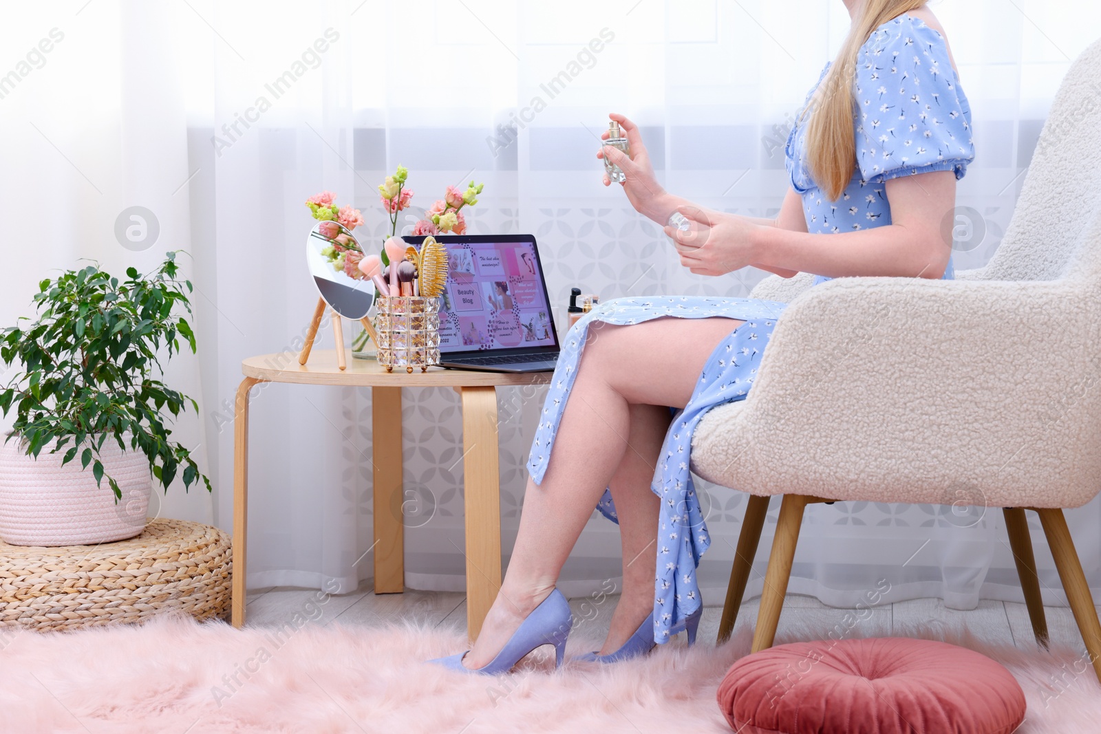 Beauty blogger spraying perfume near table with laptop and makeup products indoors, closeup Photo of Beauty blogger spraying perfume near table with laptop and makeup products indoors, closeup