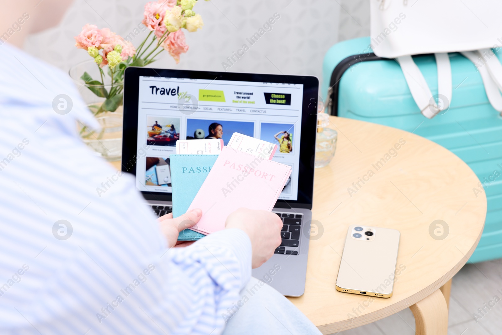 Travel blogger holding passports and flight tickets near table with laptop indoors, closeup Photo of Travel blogger holding passports and flight tickets near table with laptop indoors, closeup
