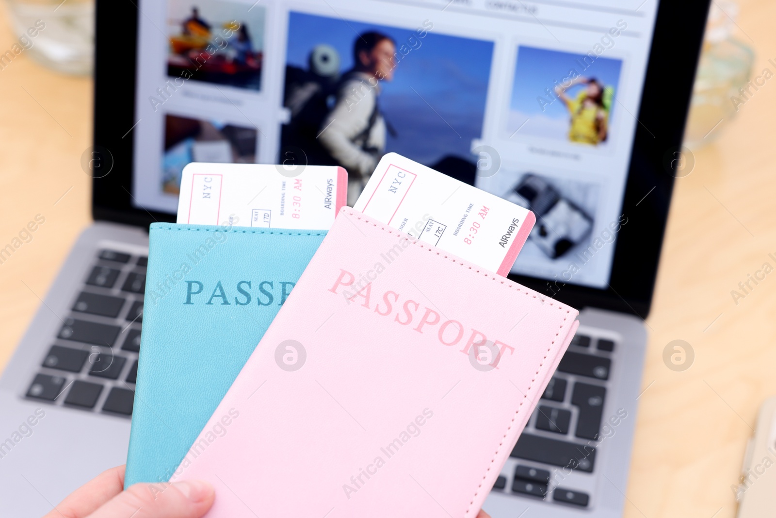 Travel blogger holding passports and flight tickets near table with laptop indoors, closeup Photo of Travel blogger holding passports and flight tickets near table with laptop indoors, closeup