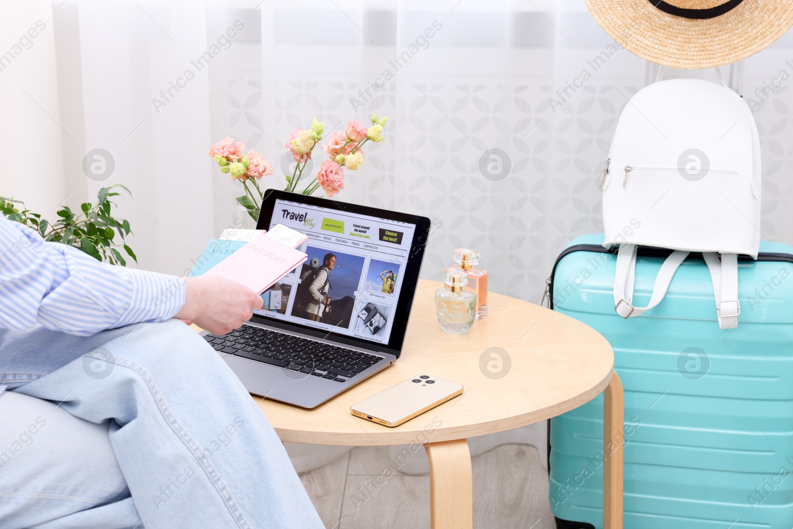 Travel blogger holding passports and flight tickets near table with laptop indoors, closeup Photo of Travel blogger holding passports and flight tickets near table with laptop indoors, closeup