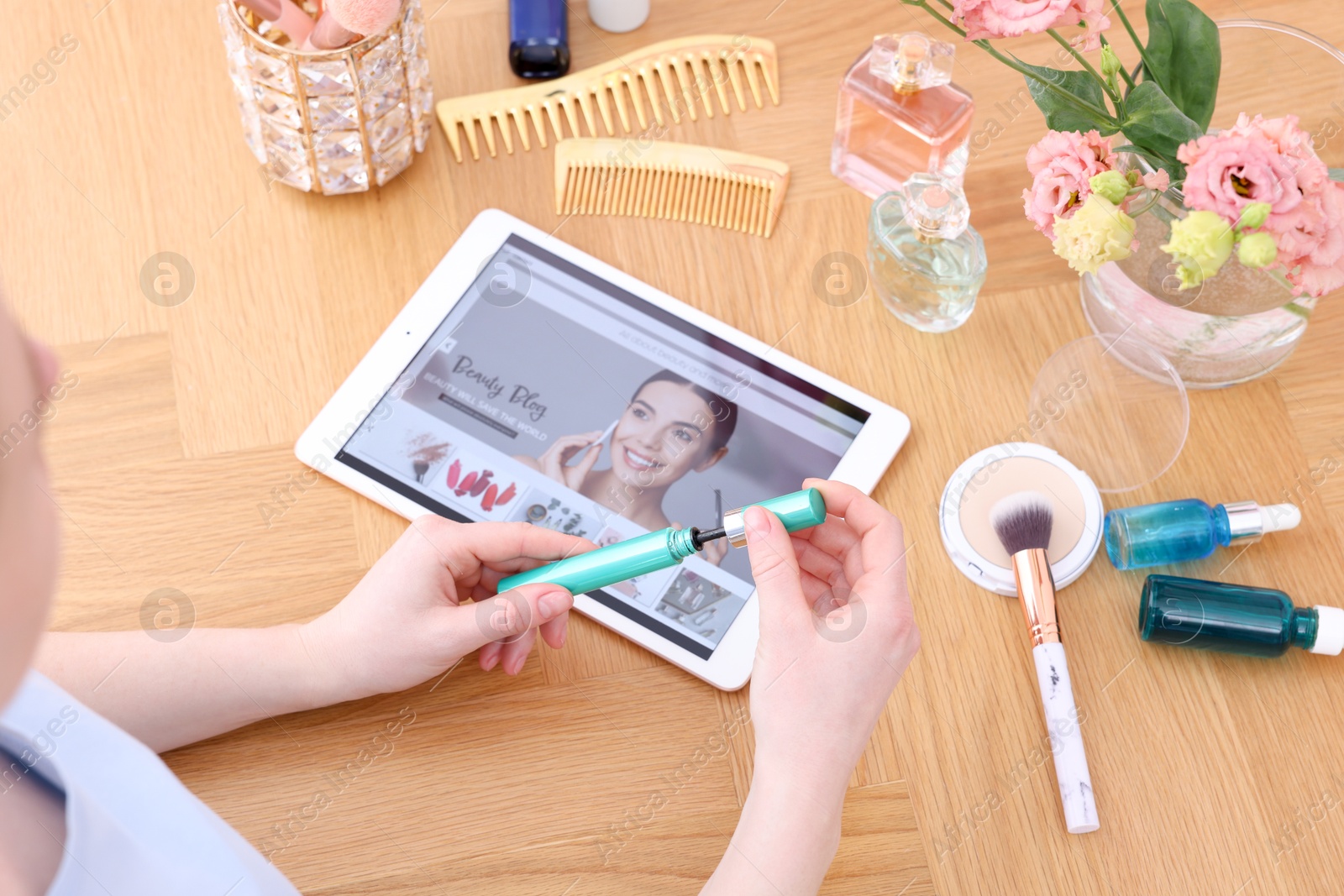 Beauty blogger holding mascara at wooden table with tablet indoors, above view Photo of Beauty blogger holding mascara at wooden table with tablet indoors, above view