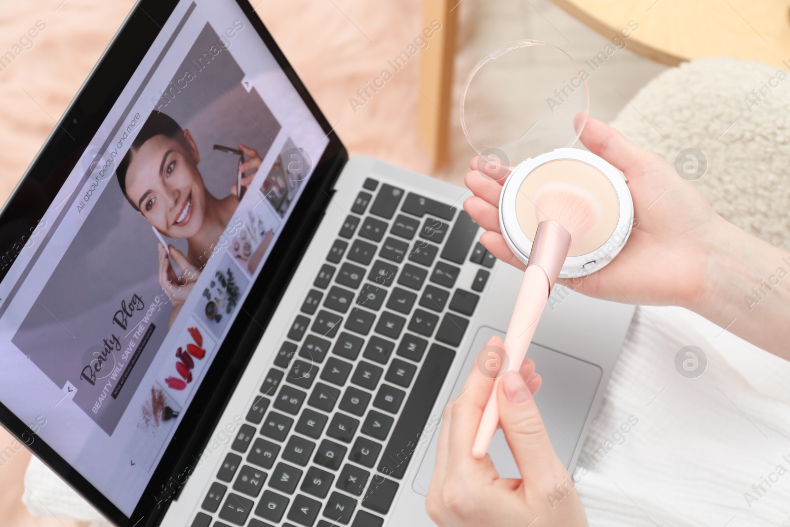 Blogger holding face powder and brush near laptop with beauty blog web site in armchair indoors, above view Photo of Blogger holding face powder and brush near laptop with beauty blog web site in armchair indoors, above view