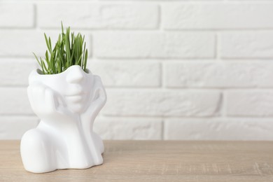Photo of Wheat grass in pot on wooden table near white brick wall. Space for text
