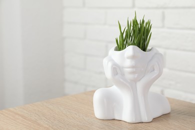 Photo of Wheat grass in pot on wooden table near white brick wall. Space for text