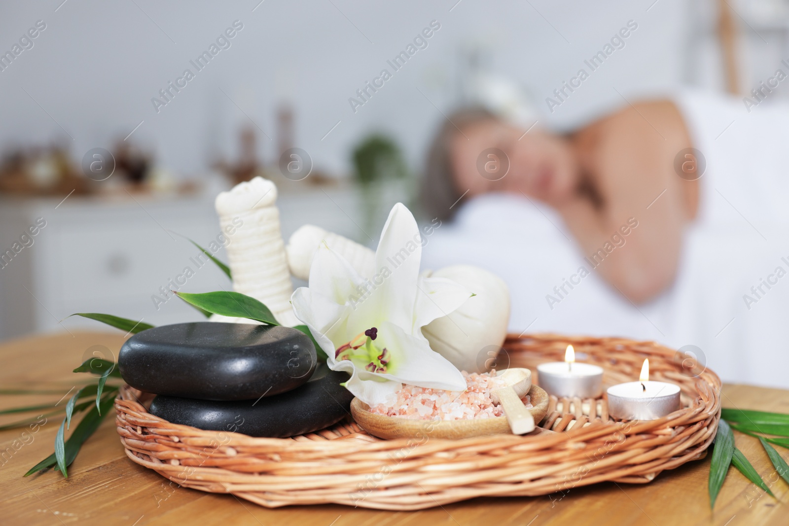 Senior woman relaxing on massage couch indoors, selective focus. Different spa products and lily flower on table Photo of Senior woman relaxing on massage couch indoors, selective focus. Different spa products and lily flower on table
