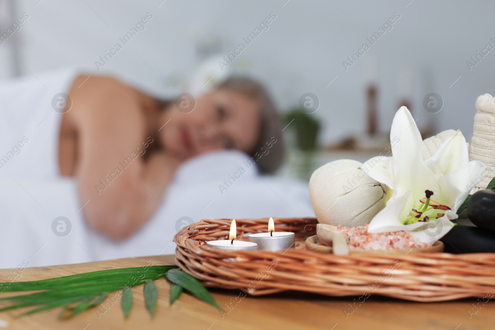 Senior woman relaxing on massage couch indoors, selective focus. Different spa products and lily flower on table Photo of Senior woman relaxing on massage couch indoors, selective focus. Different spa products and lily flower on table