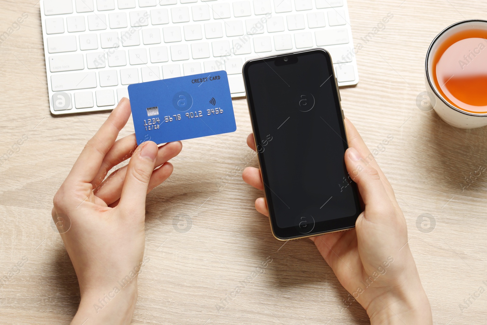 Photo of Woman with credit card and smartphone paying online at wooden table, top view