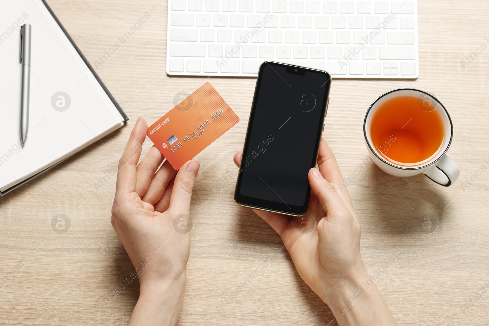 Photo of Woman with credit card and smartphone paying online at wooden table, top view