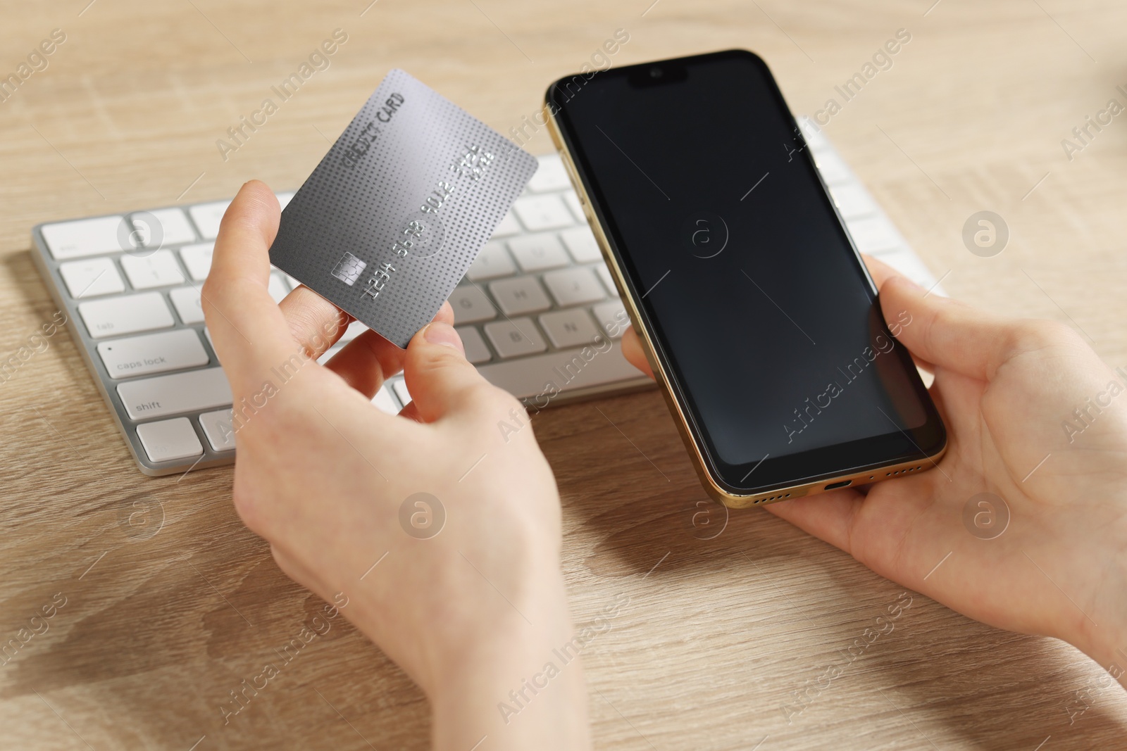 Photo of Woman with credit card and smartphone paying online at wooden table, closeup
