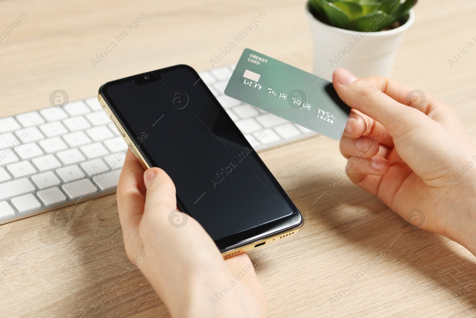 Photo of Woman with credit card and smartphone paying online at wooden table, closeup