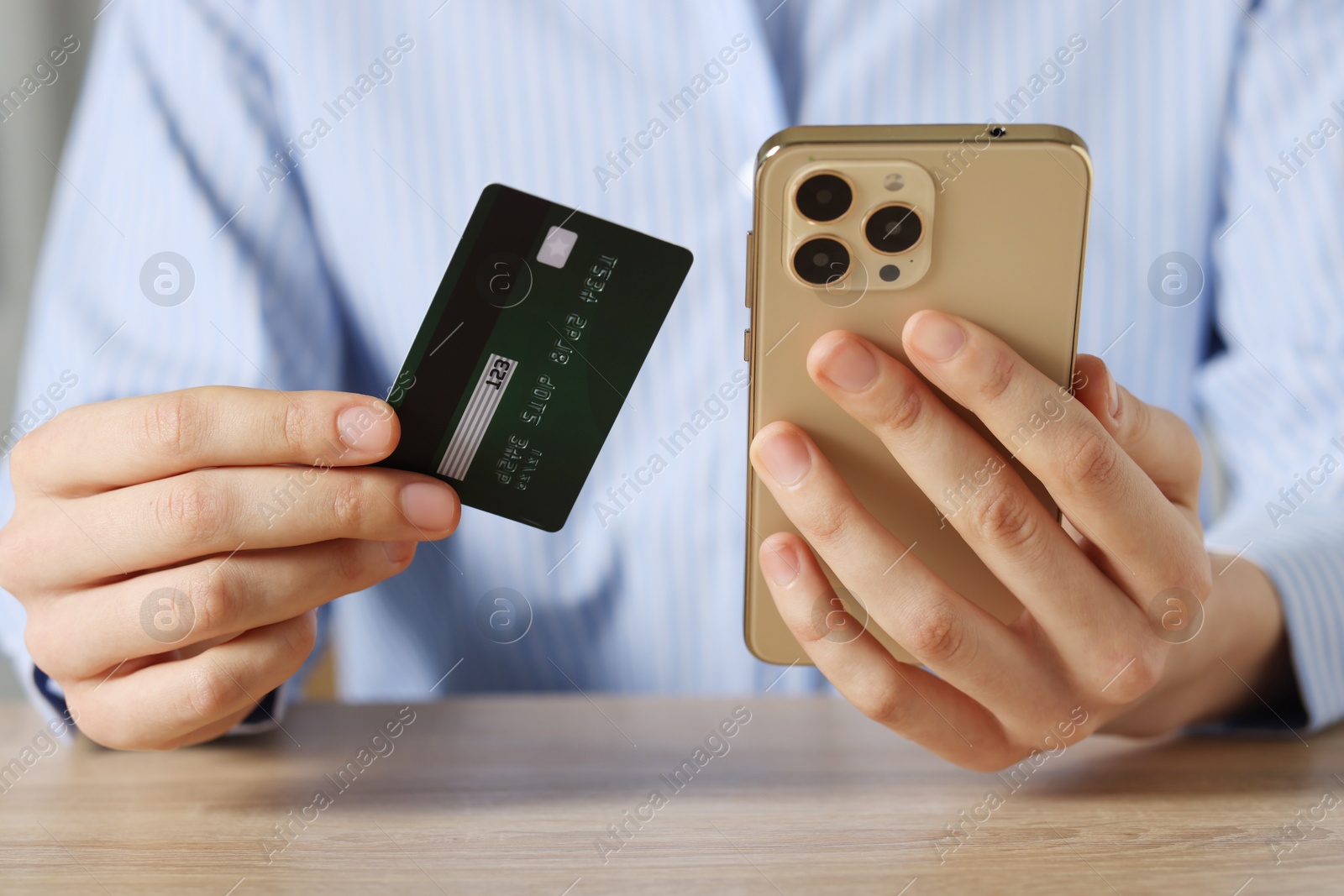 Photo of Woman with credit card and smartphone paying online at wooden table, closeup