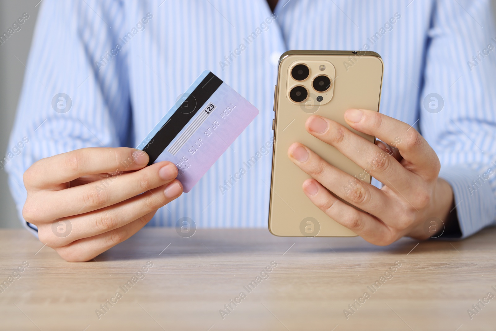 Photo of Woman with credit card and smartphone paying online at wooden table, closeup