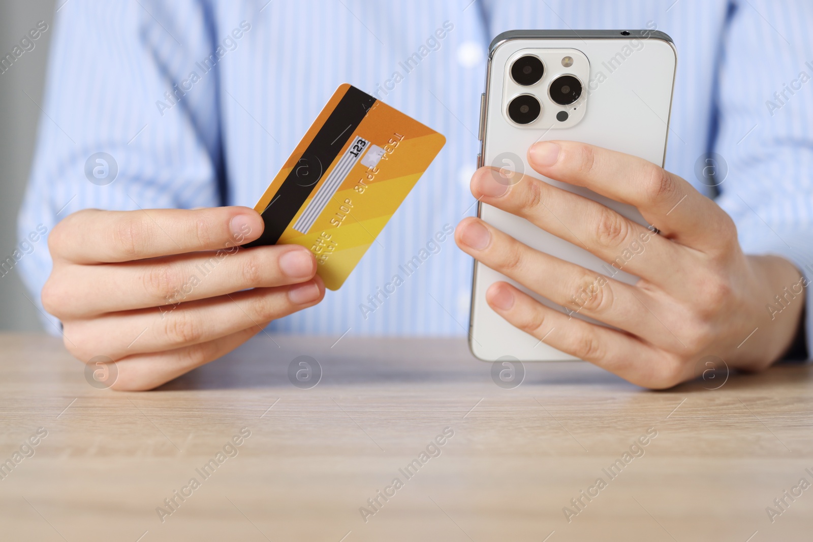 Photo of Woman with credit card and smartphone paying online at wooden table, closeup