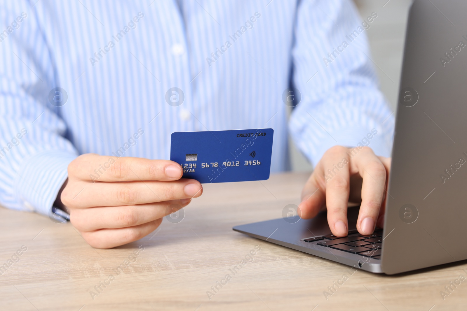 Photo of Online payment. Woman with credit card typing on laptop at wooden table, closeup