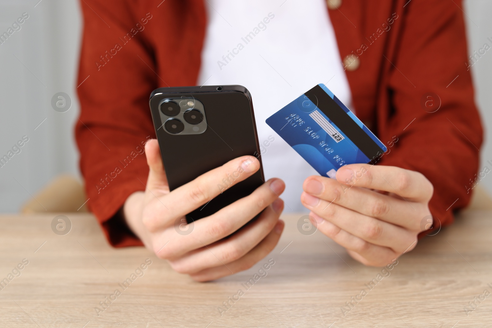 Woman with credit card and smartphone paying online at wooden table, closeup Photo of Woman with credit card and smartphone paying online at wooden table, closeup