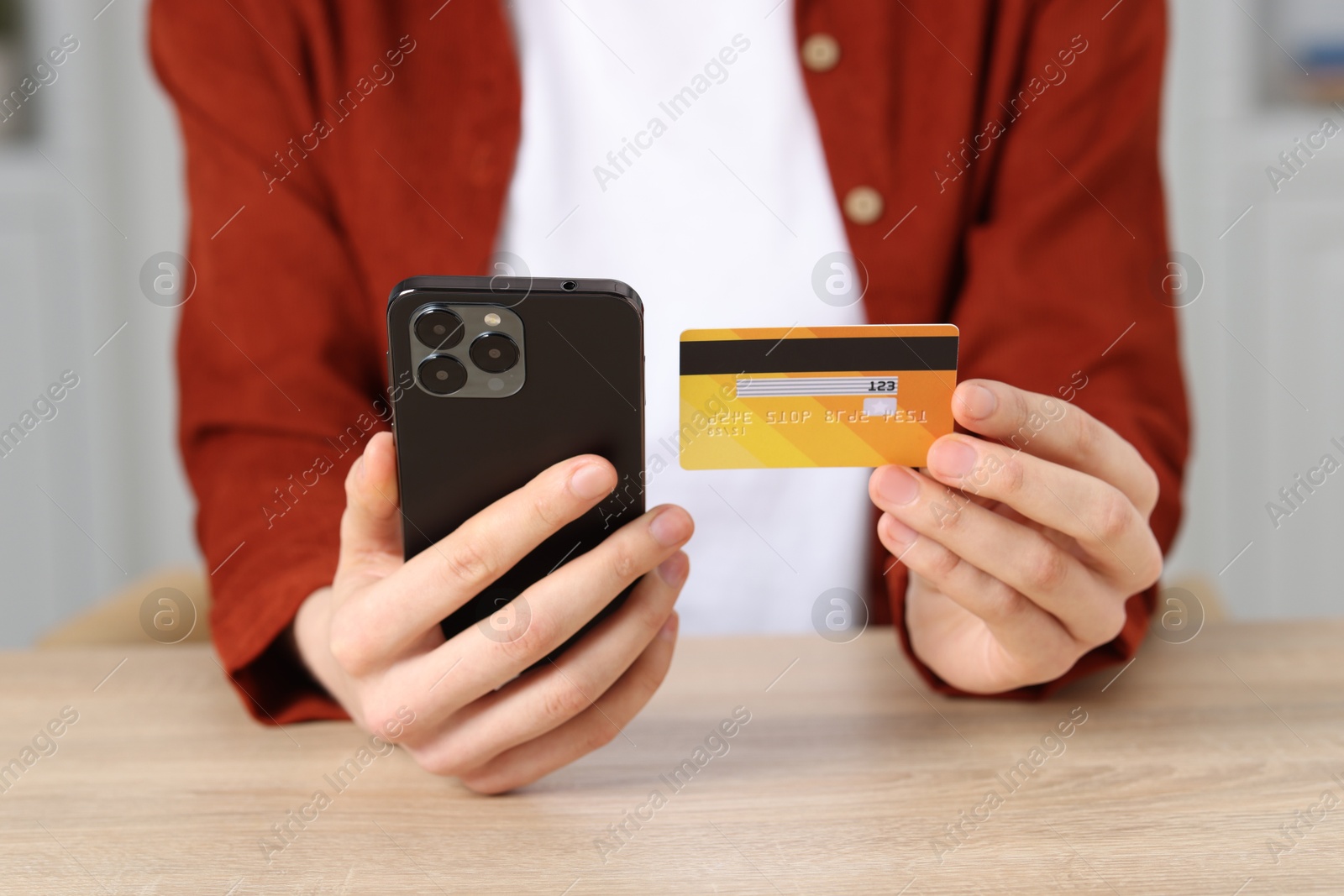 Photo of Woman with credit card and smartphone paying online at wooden table, closeup