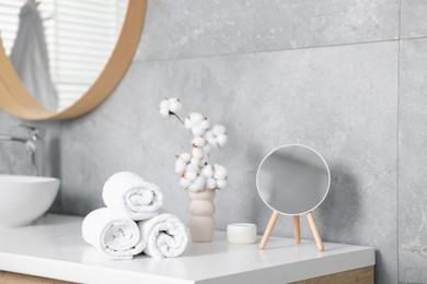 Photo of Clean towels, cotton flowers, cosmetic product and mirror on vanity in bathroom