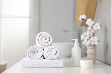 Photo of Clean towels, cotton flowers and cosmetic products on vanity in bathroom
