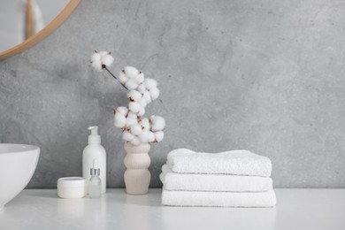 Photo of Stack of clean towels, cosmetic products and cotton flowers on vanity in bathroom