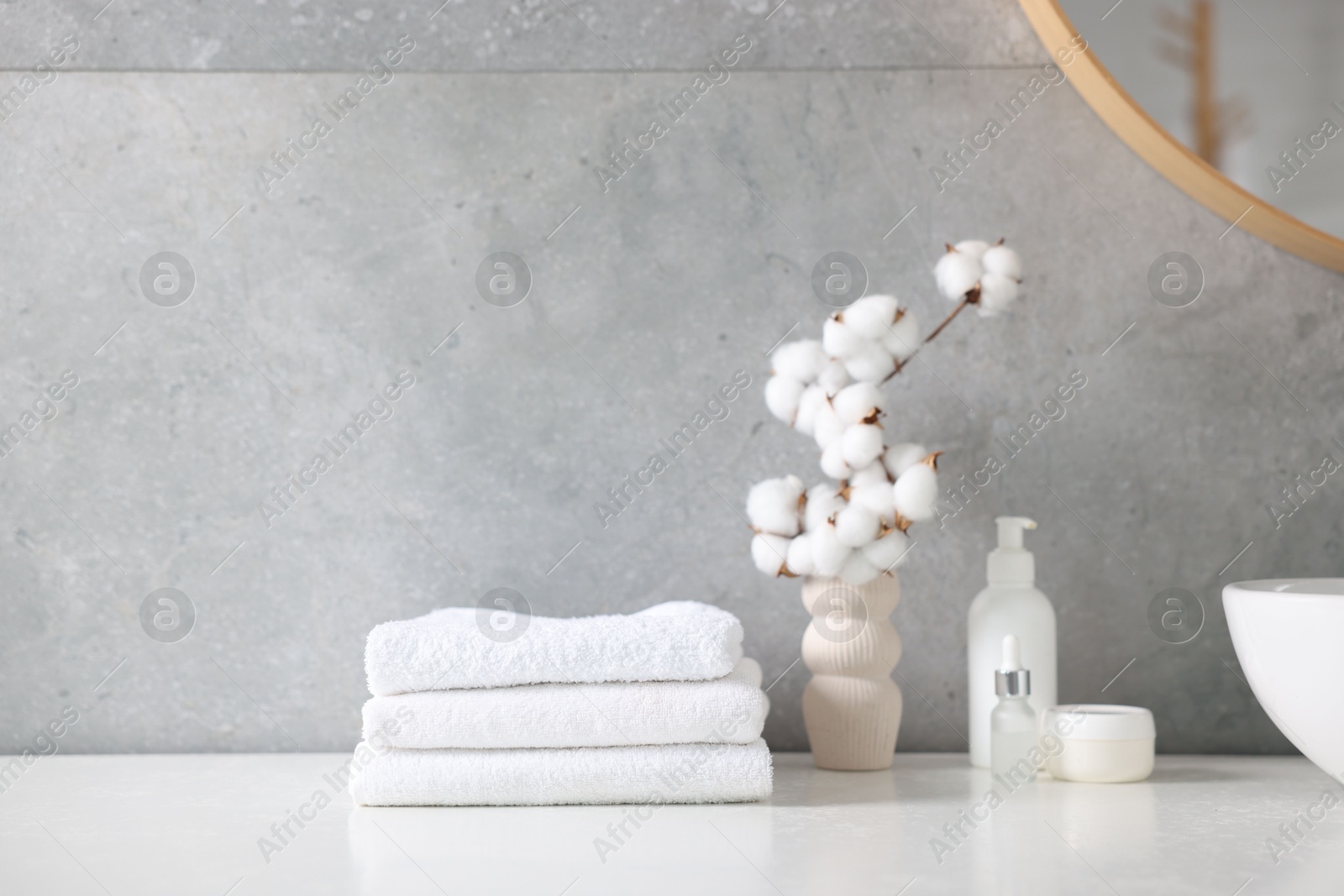 Stack of clean towels, cosmetic products and cotton flowers on vanity in bathroom Photo of Stack of clean towels, cosmetic products and cotton flowers on vanity in bathroom