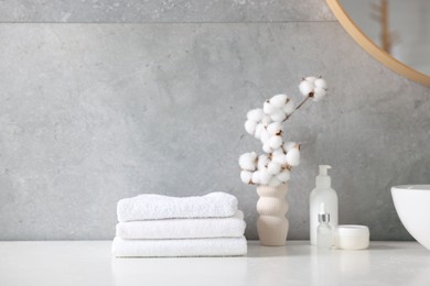 Photo of Stack of clean towels, cosmetic products and cotton flowers on vanity in bathroom