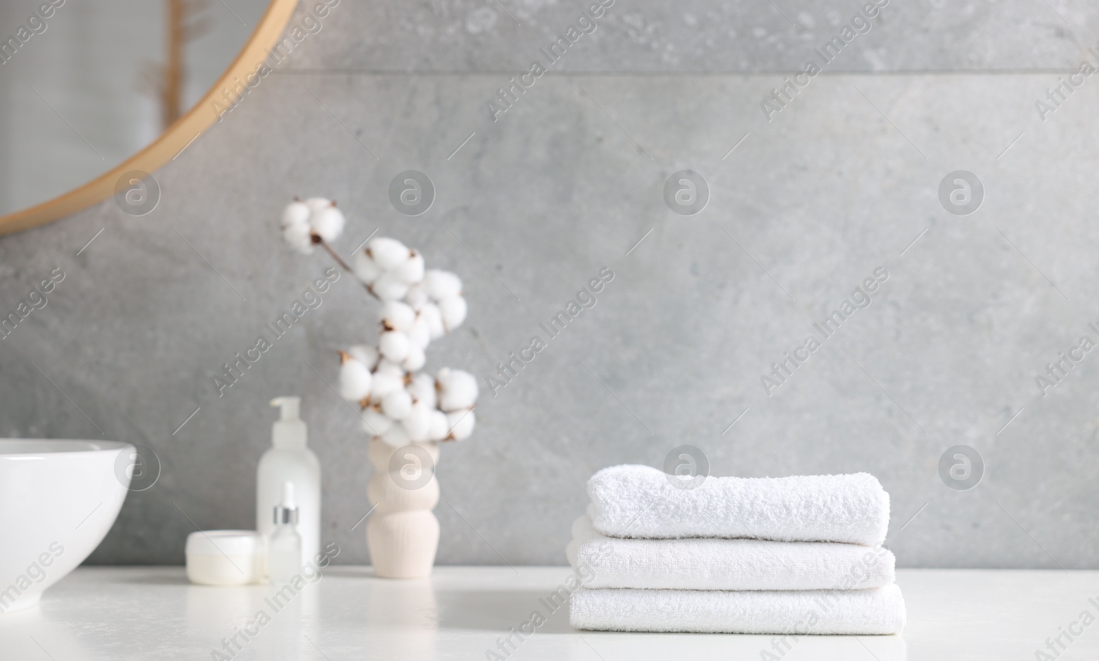Stack of clean towels, cosmetic products and cotton flowers on vanity in bathroom Photo of Stack of clean towels, cosmetic products and cotton flowers on vanity in bathroom