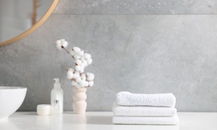 Photo of Stack of clean towels, cosmetic products and cotton flowers on vanity in bathroom