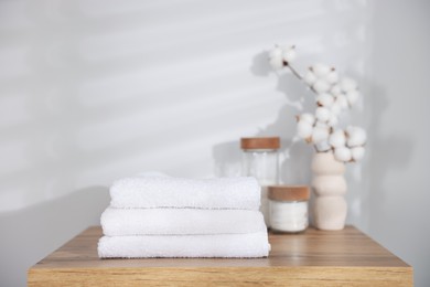 Photo of Stack of clean towels, cotton flowers and pads on wooden table indoors