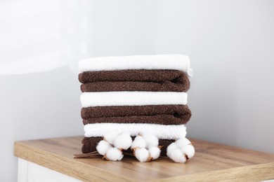 Photo of Stack of clean towels and cotton flowers on wooden cabinet indoors