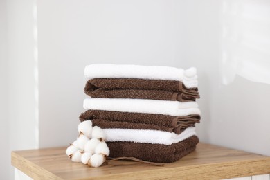 Photo of Stack of clean towels and cotton flowers on wooden cabinet indoors