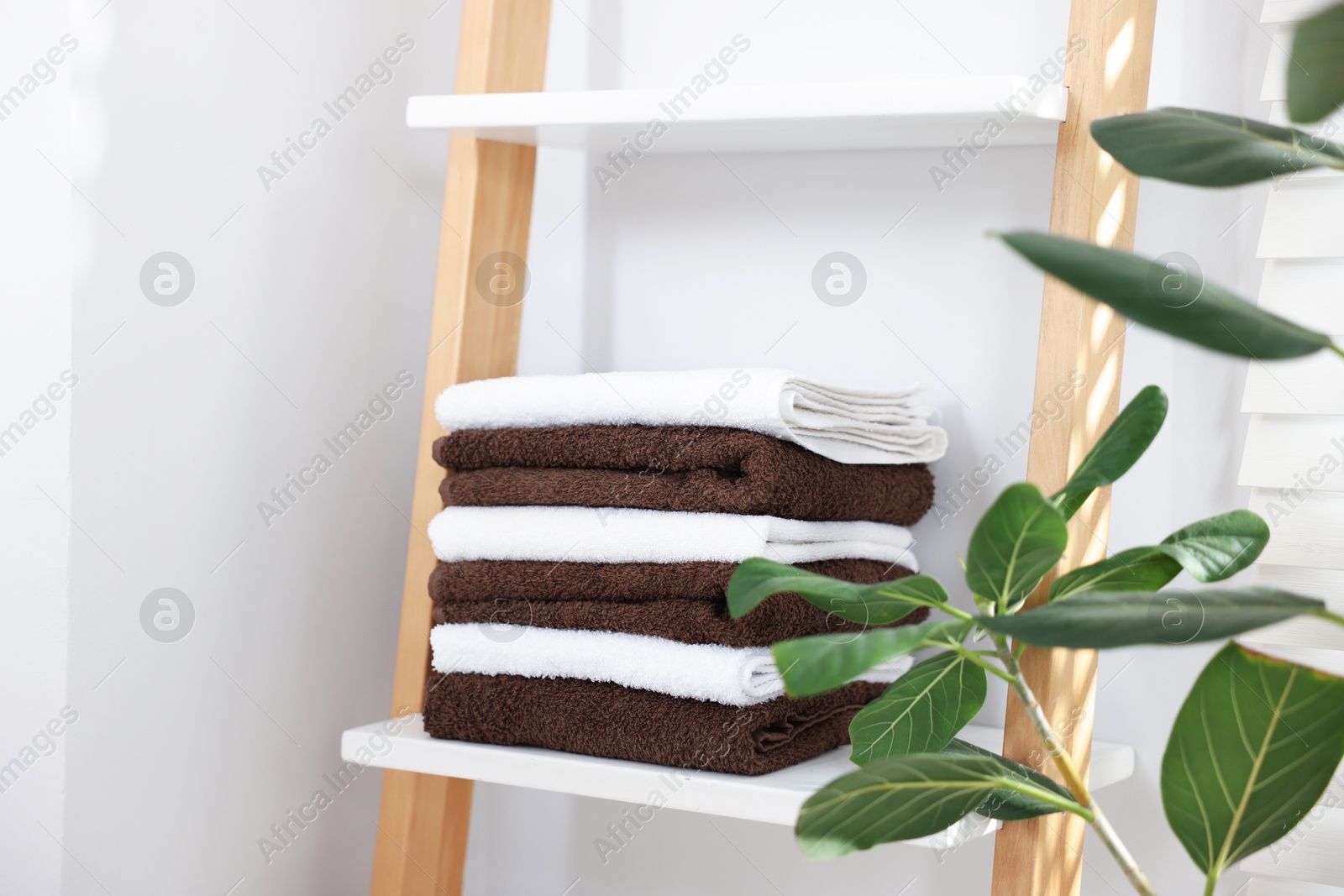 Stack of clean towels on white shelf and houseplants indoors Photo of Stack of clean towels on white shelf and houseplants indoors