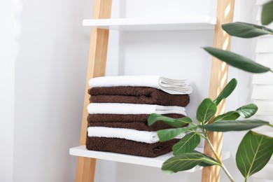 Photo of Stack of clean towels on white shelf and houseplants indoors