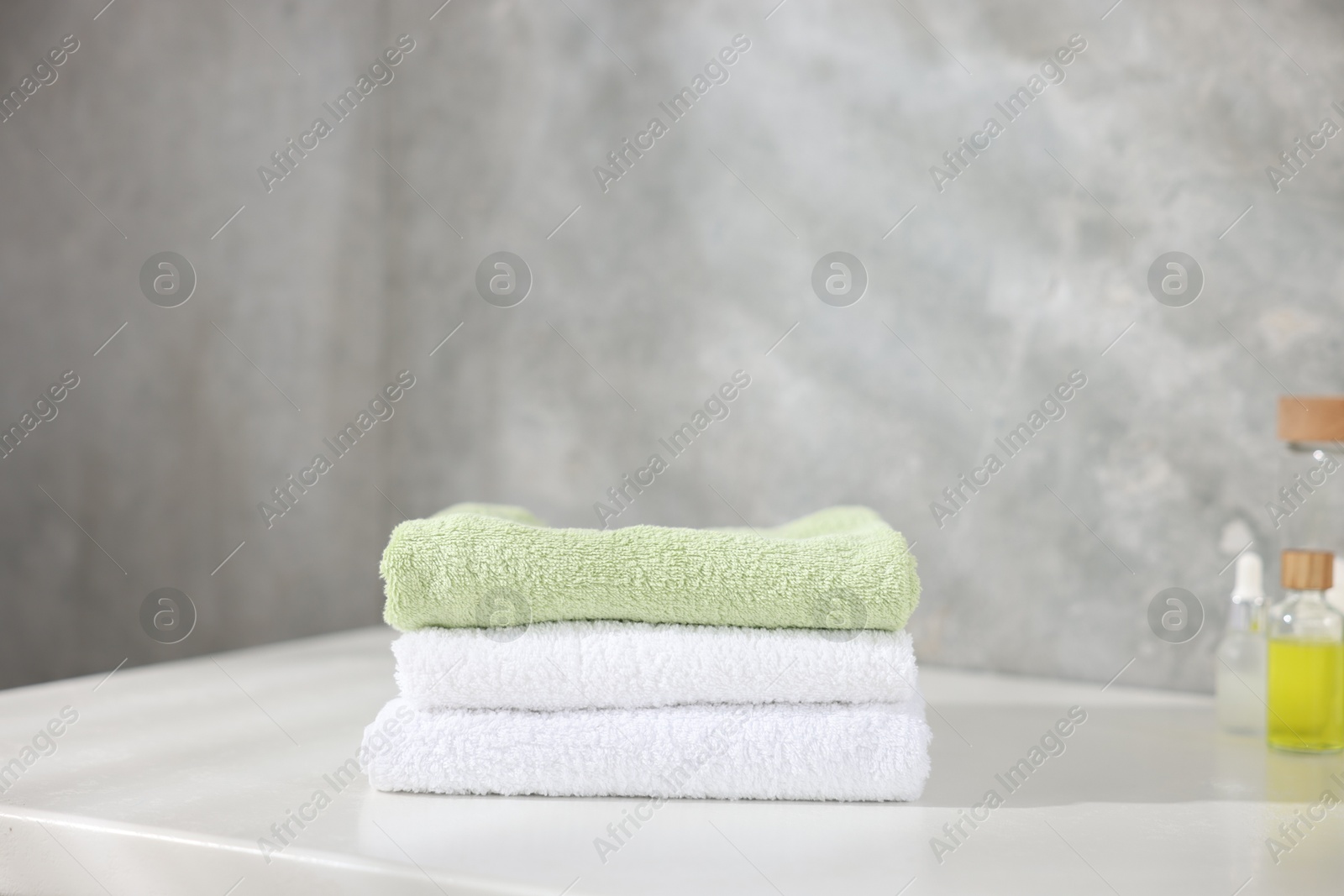 Stack of clean towels and cosmetic products on white table indoors Photo of Stack of clean towels and cosmetic products on white table indoors