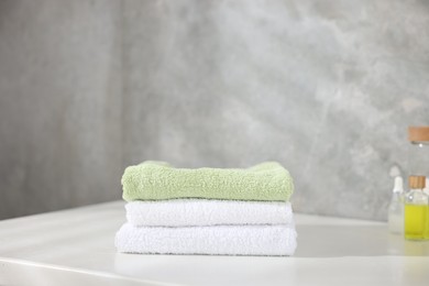 Photo of Stack of clean towels and cosmetic products on white table indoors