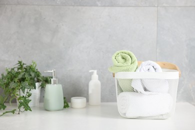 Photo of Clean towels in basket, cosmetic products and houseplant on white table indoors
