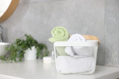 Photo of Clean towels in basket, cosmetic products and houseplant on vanity indoors