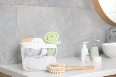 Photo of Clean towels in basket, cosmetic products and brush on vanity indoors