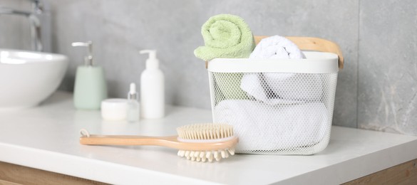 Photo of Clean towels in basket, cosmetic products and brush on vanity indoors